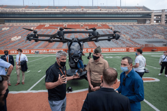 Marine General Gary Thomas, a 1984 graduate of UT Austin, listens to information about the capabilities and potential uses of a car-sized eVTOL aircraft developed by LIFT Aircraft (seen in background).